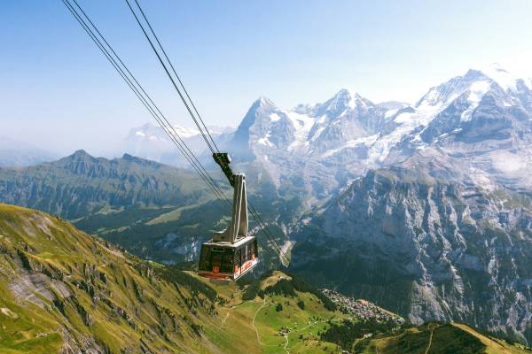 Cable car rising above snow-capped mountains with green fields beneath in Switzerland