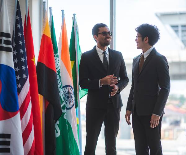 Two diplomats talking in front of an array of flags