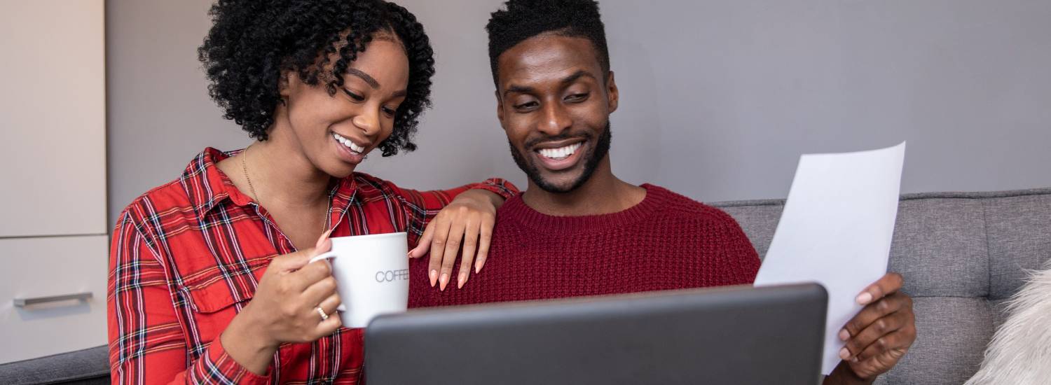Smiling couple looking at a laptop and holding a piece of paper