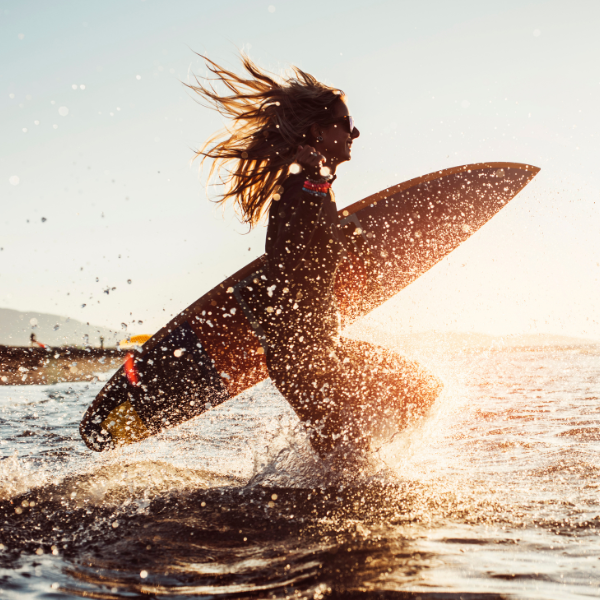 Woman running in the ocean with a surfboard