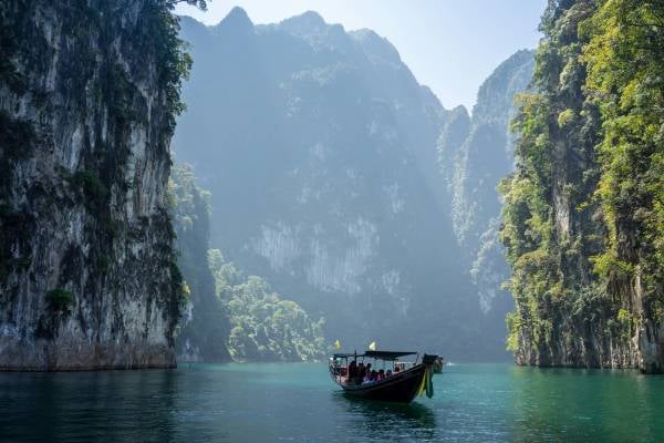 Boat on a blue sea between tree covered cliffs in Thailand