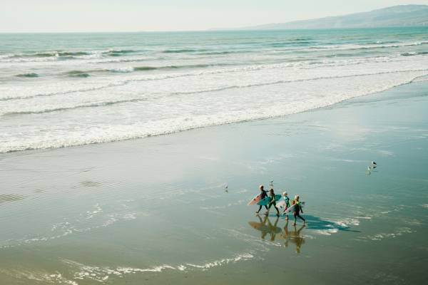 People walking along a sandy beach holding surfboards in New Zealand