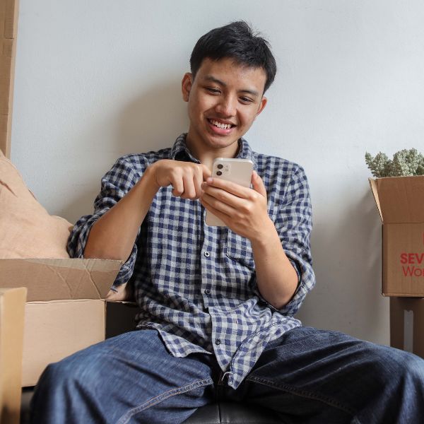 Man using his phone while sitting beside packed moving boxes