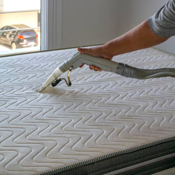 Someone holding a vacuum cleaner and using it to clean a mattress