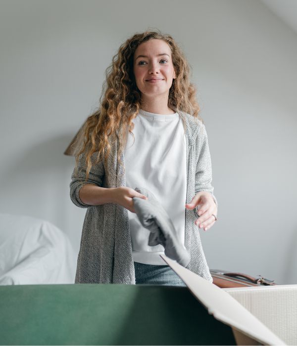 Woman packing clothes and personal belongings into a cardboard moving box.