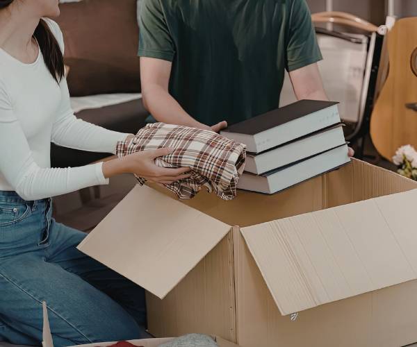 Couple packing books and clothes into a cardboard box