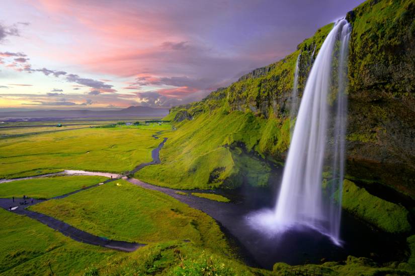 Seljalandsfoss Waterfall pouring from a verdant green cliff at dusk in Iceland