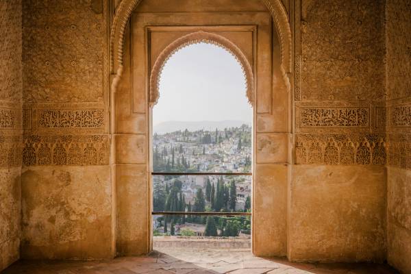Looking through an ornate arch at a village on a hill in Spain