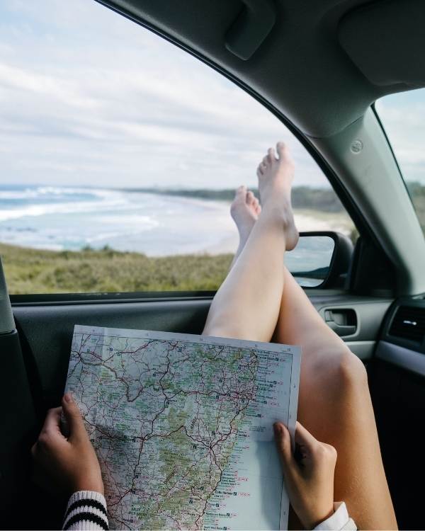 Woman sitting with her legs out of a car window holding a map