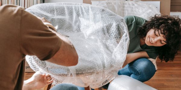 Two people wrapping a chair in bubble wrap while packing household belongings for an international move